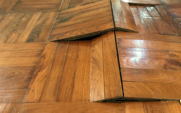Water damaged wooden parquet flooring buckling due to moisture.